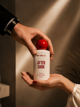 A person in a black suit sleeve hands a bottle of BA BE LL AFTER DARK Eau De Parfum to another person&
