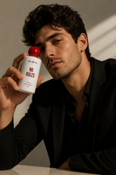 A man in a black suit jacket holds a white bottle of BA BE LL &